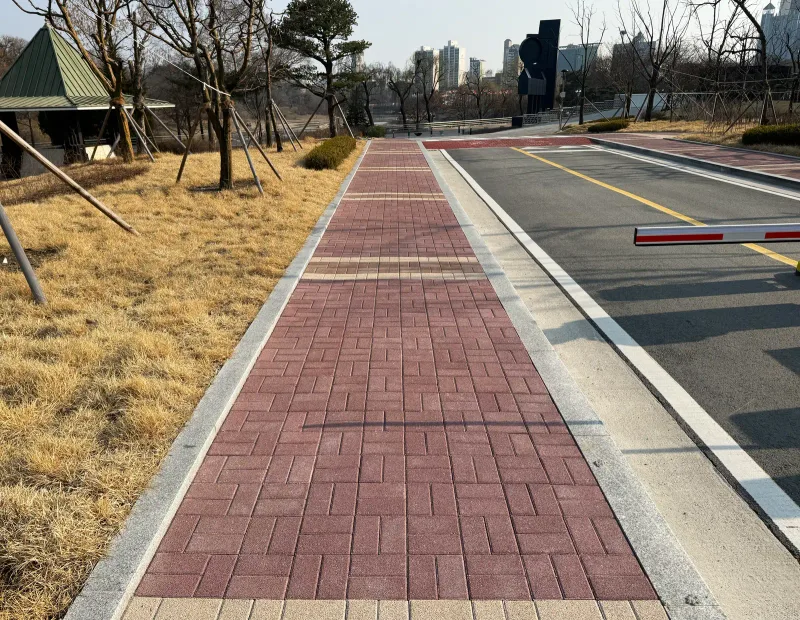올림픽회관 차량 출입로 옆 보행로. 적갈색 블록 길이 경계석을 따라 곧게 뻗고 오른쪽에 차단기가 보인다.