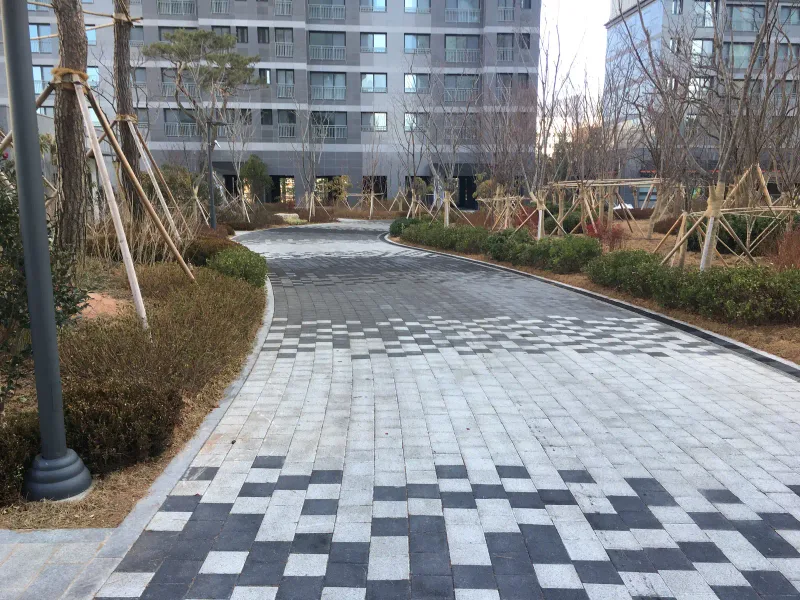 창원 용호 더샵 동 사이로 굽어 드는 보행로. 밝은 회색 블록 바탕 앞쪽에 짙은 회색 블록이 흩어져 박혀 그러데이션을 이룬다.