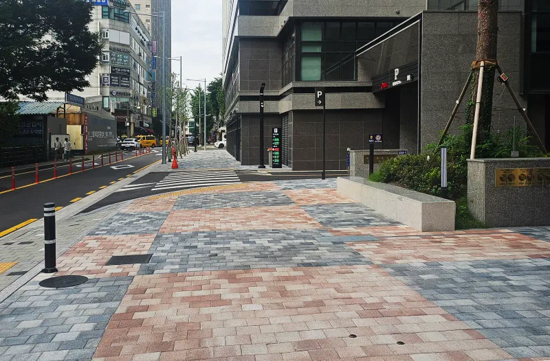 도봉 롯데캐슬 가로변 보도 접속부. 분홍빛 블록과 청회색 블록이 섞여 깔린 보도 끝에 볼라드가 서 있고 오른쪽으로 화단과 건물 입구가 보인다.