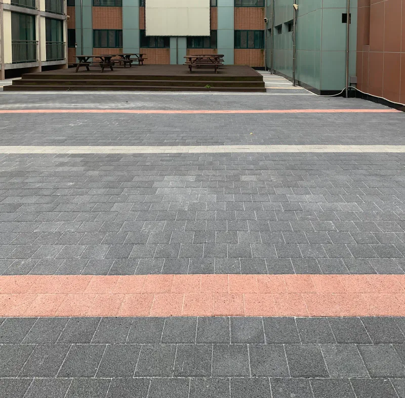 한국체육고등학교 중정 휴게 공간. 짙은 회색 블록 바닥에 분홍·밝은 회색 띠가 나란히 깔려 있고 뒤로 목재 데크와 탁자가 보인다.