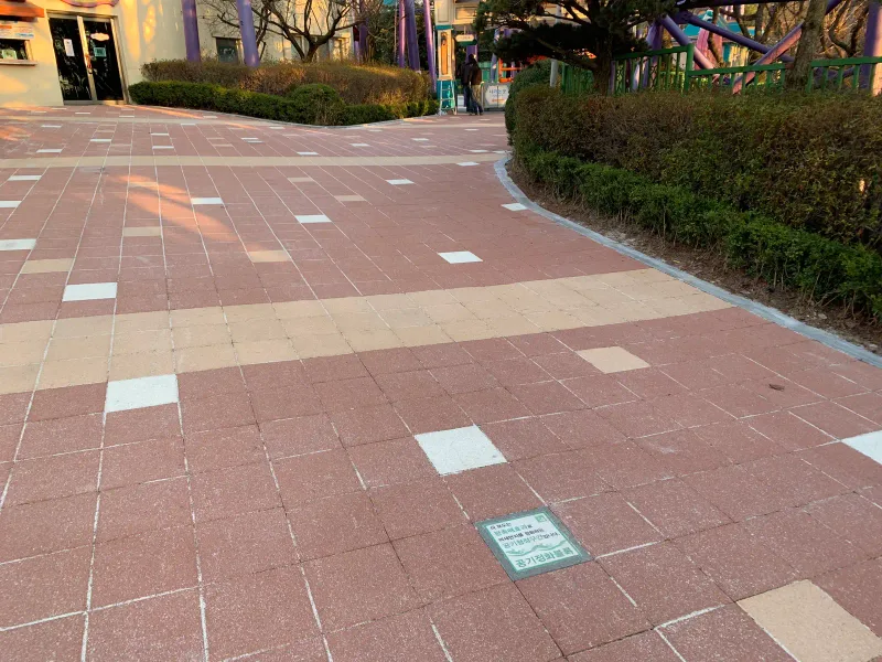 서울랜드 보행로 바닥. 적갈색 블록 사이로 베이지 블록 띠와 흰 블록이 놓이고 공기정화블록 안내판이 바닥에 매립되어 있다.