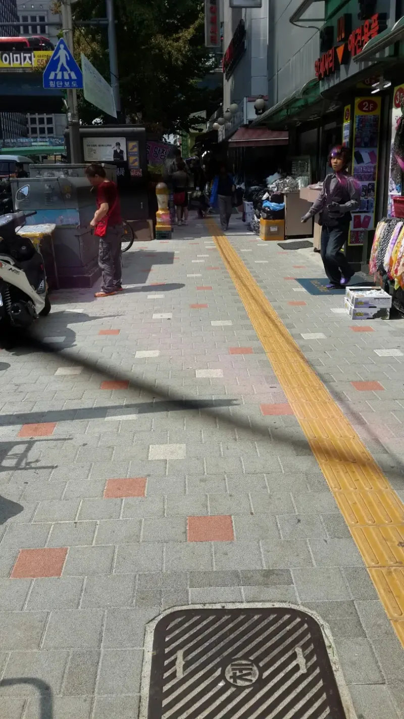 남대문시장 상가 거리 보도. 연회색 사각 블록 사이에 주황빛 적색 블록과 흰 블록이 흩어져 박혀 있고 가운데로 노란 점자블록이 길게 이어진다.