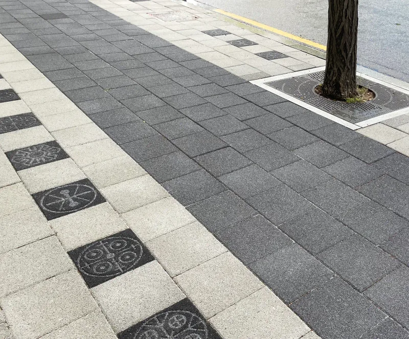 천호대로 가로수 보호덮개 주변. 짙은 회색 블록 보행면과 연회색 띠의 경계를 따라 문양 블록이 박힌 모습을 가까이에서 본 사진.