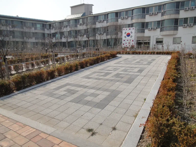 수원보훈원 건물 앞 넓은 보행로. 밝은 회색 블록에 짙은 회색 번개무늬가 연속으로 들어가 있고 끝에 태극기 조형물과 건물이 있다.