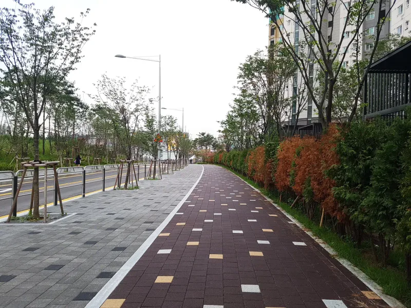 신길 래미안 단지 옆 보행로. 회색 블록 보도 옆으로 적갈색 바탕에 밝은 블록이 흩어진 길이 붉게 물든 생울타리를 따라 이어진다.