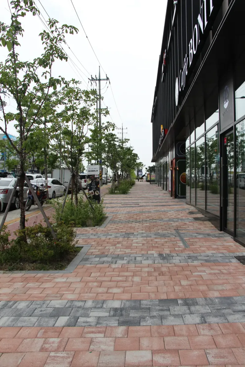 마치에비뉴 2차 가로변 보도 세로 사진. 분홍빛·회색 블록이 깔린 길 옆으로 가로수와 화단이 줄지어 있다.