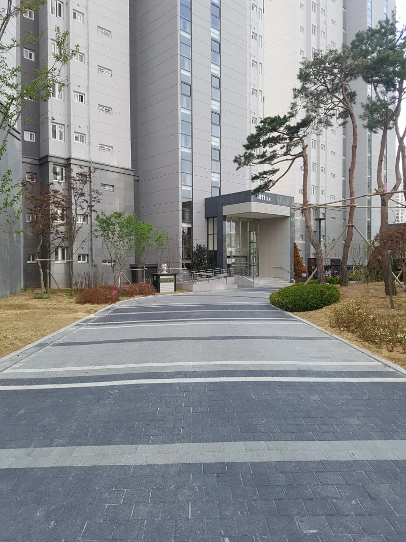 시흥 배곧 한신휴플러스 동 출입구로 이어지는 곧은 길. 짙은 회색 블록 바탕에 밝은 회색 가로 띠가 간격을 두고 반복된다.