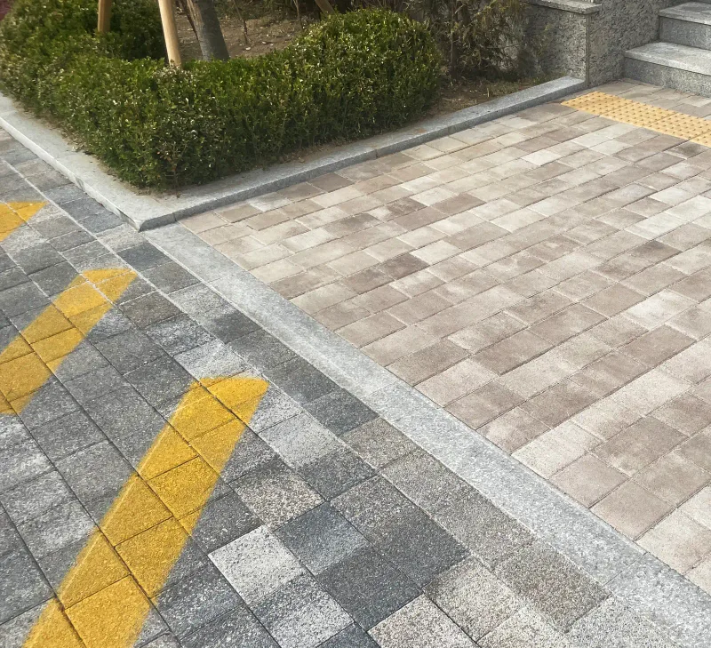 위례 자이 더 시티 보도 접속부. 회색 블록 위 노란 노면 표시 옆으로 베이지 블록 보도가 이어지고 모서리에 점자블록과 계단이 보인다.