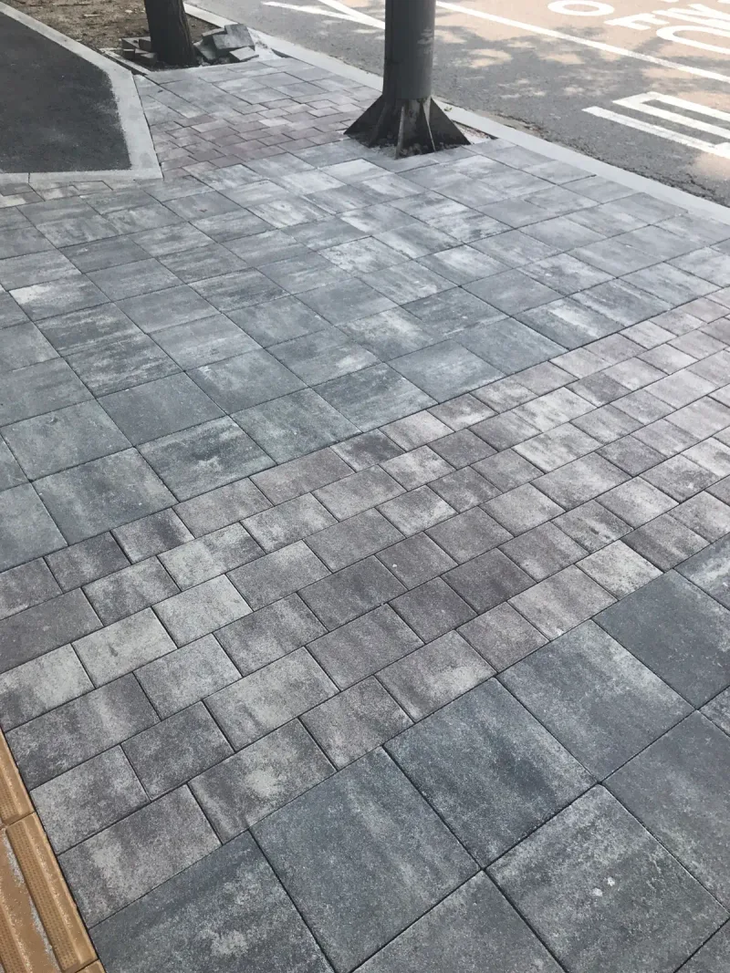 잠실관광특구 가로수 주변 세로 사진. 회색·흰색 블록이 나무 둘레를 감싸고 앞쪽으로 노란 점자블록이 이어진다.