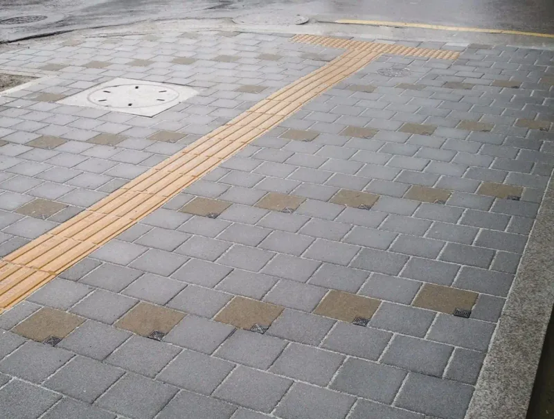 사당로 시범공사구간 보도. 짙은 회색 블록 사이로 작은 배수 덮개가 박힌 베이지 블록이 일정 간격으로 놓이고, 노란 점자블록 띠가 비스듬히 지난다.