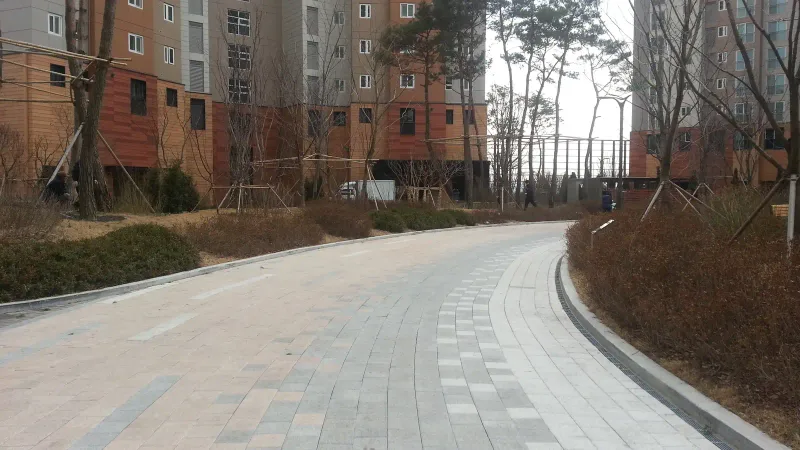 영통 래미안 마크원 단지 안 곡선 차로. 베이지·분홍빛과 회색·흰색 블록이 길 방향으로 색 띠를 이루며 완만하게 휘어지고, 양옆 화단 너머로 아파트 동이 서 있다.