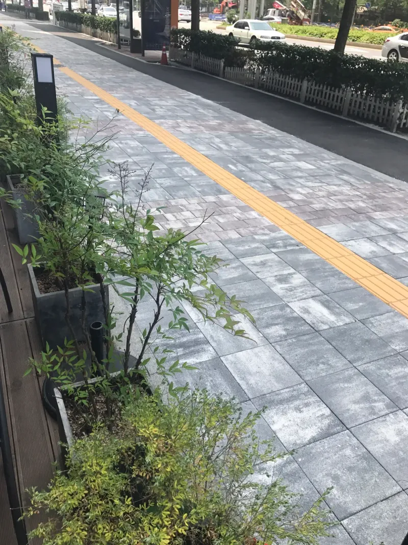 잠실관광특구 상가 앞 보도 세로 사진. 나무 화분과 기둥형 조명을 따라 회색 계열 블록 보도와 노란 점자블록이 멀리 이어진다.