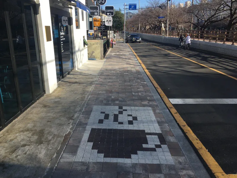 동래온천 카페거리 상가 앞 보도. 흰색과 짙은 갈색 정사각형 블록으로 만든 커피잔 무늬가 블렌딩 톤 블록 사이에 놓여 있다.
