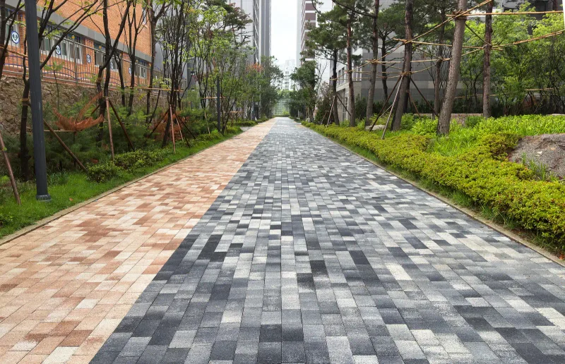 올림픽파크포레온 동 사이 보행로. 왼쪽 분홍·베이지 블록과 오른쪽 짙은 회색·흰색 혼합 블록이 길게 맞닿아 있고 양옆을 관목 화단이 두른다.