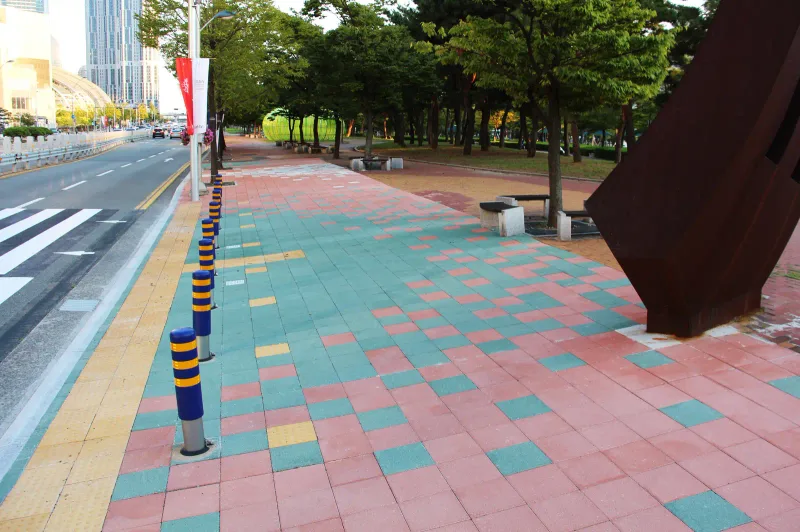 부산 영화의전당 옆 보행로. 적갈색 바탕에 청록·흰색·노란색 정사각형 블록이 모자이크처럼 흩어져 있고 녹슨 철 조형물이 놓여 있다.