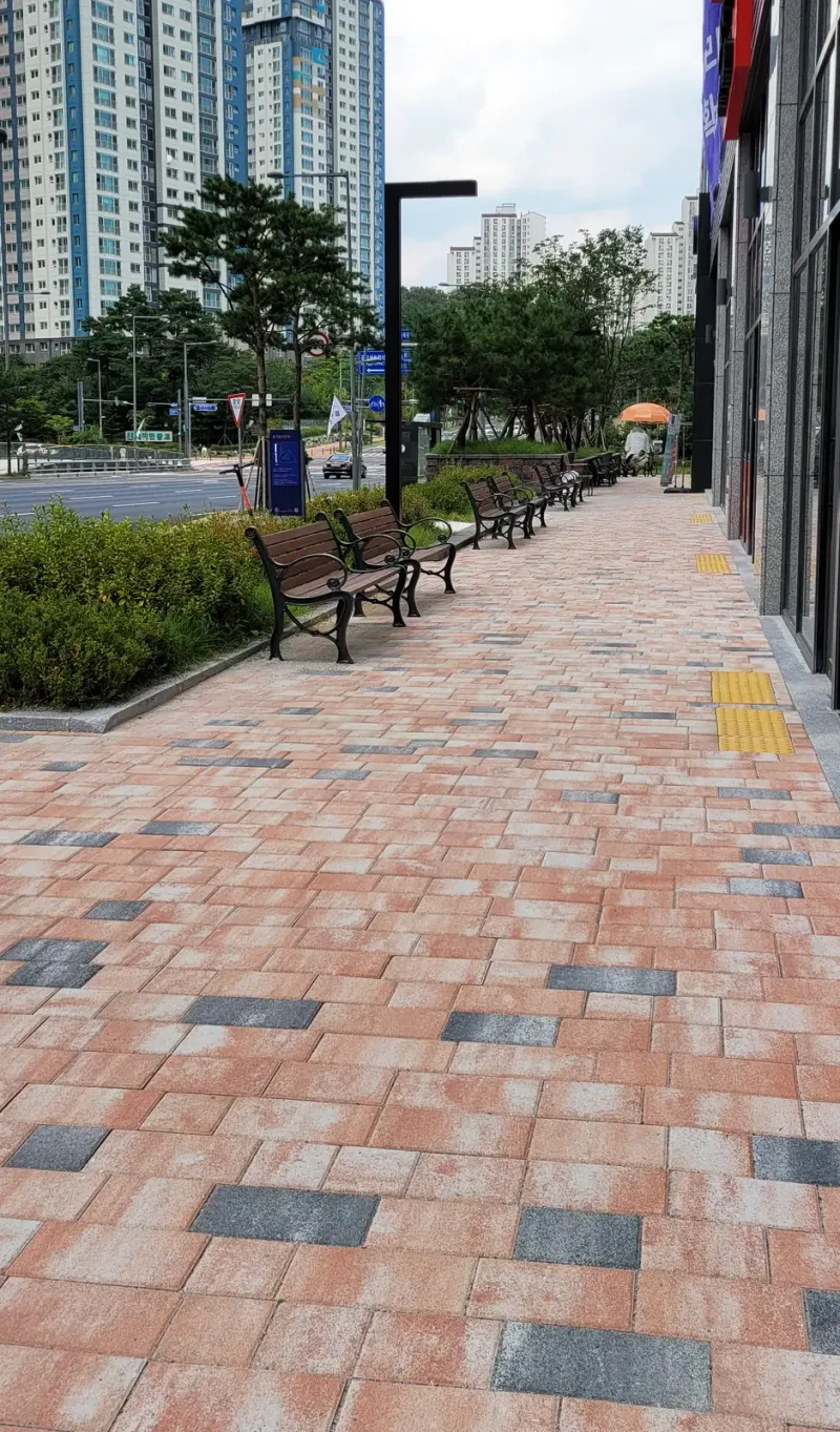 광교 효성해링턴타워 레이크 상가 앞 보행로. 분홍빛과 회색이 섞인 블록 길을 따라 벤치와 가로등이 늘어서 있고 노란 점자블록이 보인다.