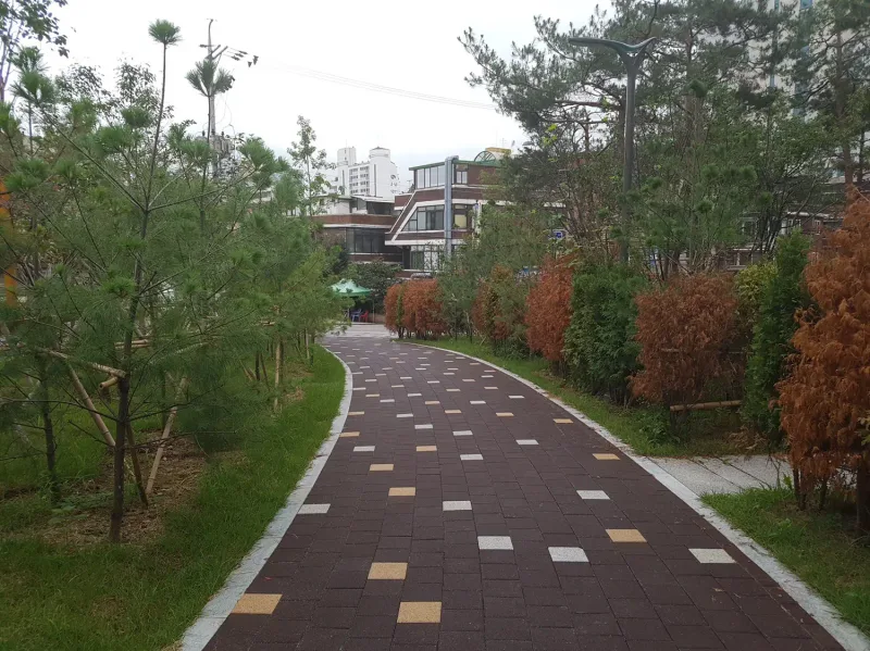 신길 래미안 단지 안 산책로. 짙은 적갈색 블록 바탕에 베이지·흰색 블록이 점점이 섞인 길이 소나무와 관목 사이로 굽어진다.