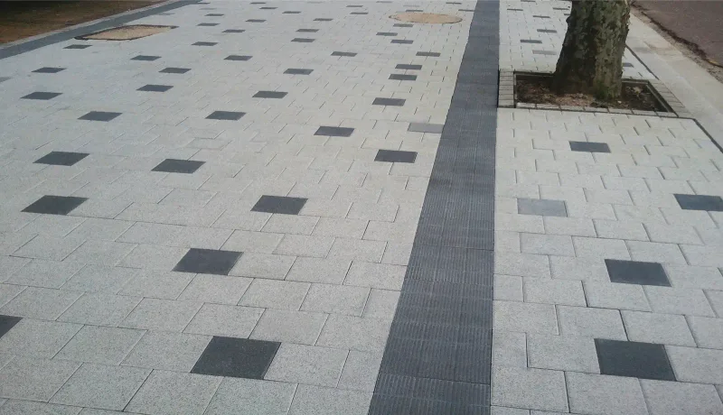 노원구 동일로 보도. 연회색 블록 바탕에 짙은 회색 정사각형 블록이 흩어져 박혀 있고, 가로수 옆으로 홈이 파인 짙은 회색 무장애띠블록이 한 줄로 길게 이어진다.
