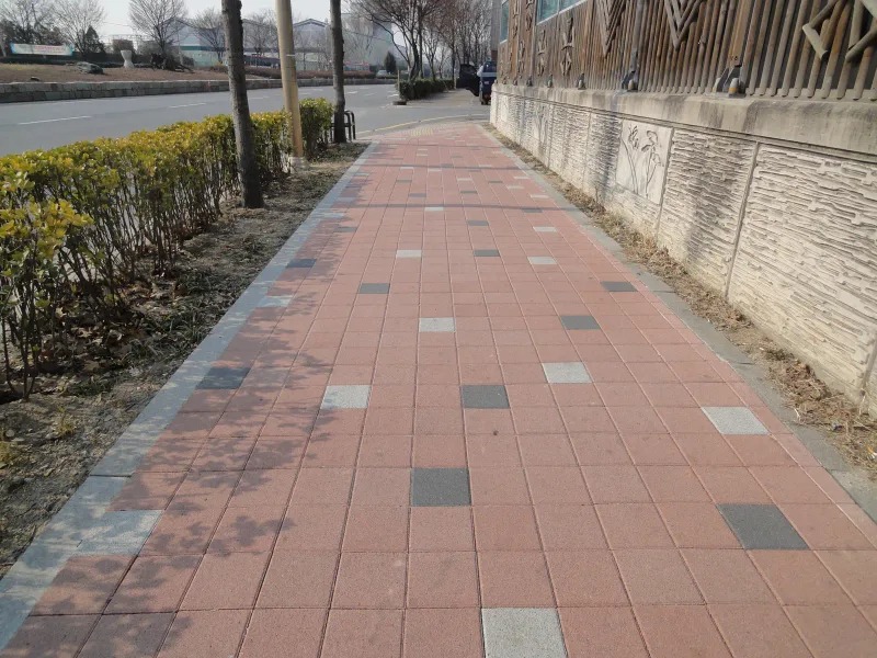 수원 세류동 보도. 분홍빛 적색 블록 바탕에 회색·짙은 회색·흰색 블록이 드문드문 섞인 보도가 무늬 옹벽과 생울타리 사이로 곧게 뻗는다.