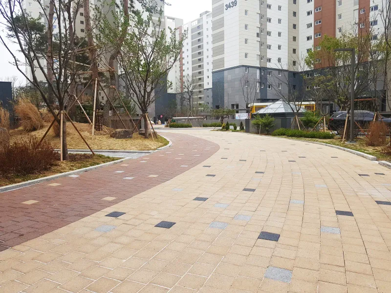 동탄2 아이파크 단지 산책로. 적갈색 띠와 베이지 블록이 나란히 곡선을 그리며 깔려 있고 검은색·회색 블록이 점점이 섞여 있다.