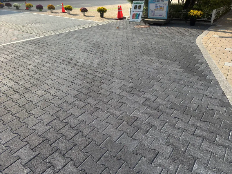마포 염리초등학교 교내 차량 통로. 짙은 회색 맞물림 블록이 넓게 깔려 있고 끝에 국화 화분과 안내판이 늘어서 있다.