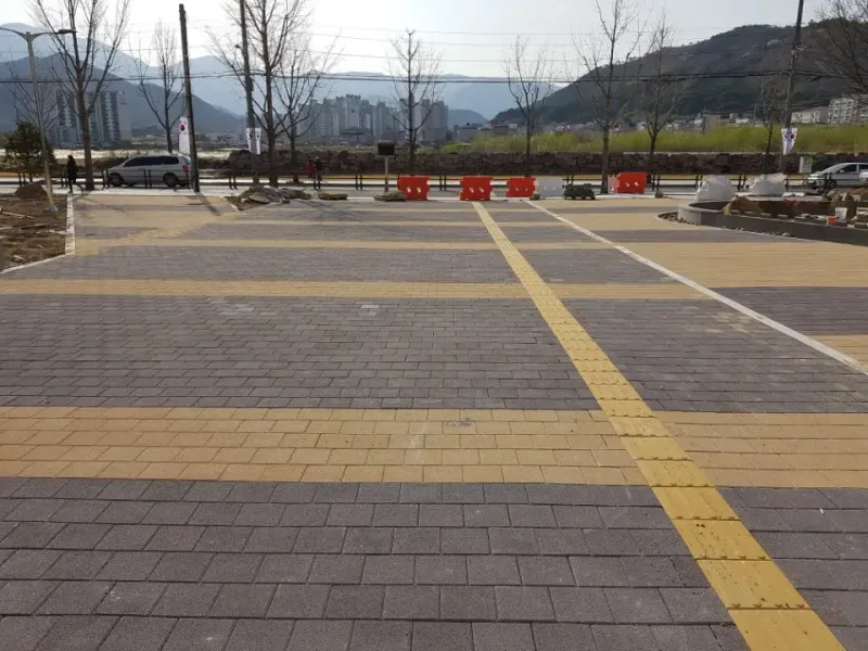언양읍 청사 광장을 도로 쪽으로 본 모습. 보랏빛 회색 블록 바닥에 베이지 띠가 격자로 지나고 점자블록이 사선으로 가로지르며 뒤로 산과 아파트가 보인다.