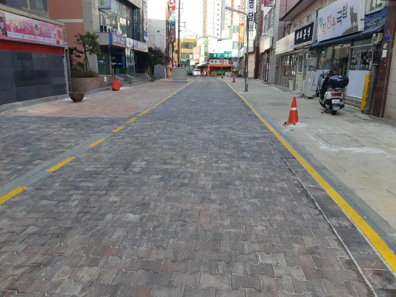 방어진 국제디자인거리 차로를 따라 본 모습. 회갈색 블렌딩 차도블록 길 양쪽에 노란 선과 배수 트렌치, 적갈색 보도가 나란히 뻗어 있다.