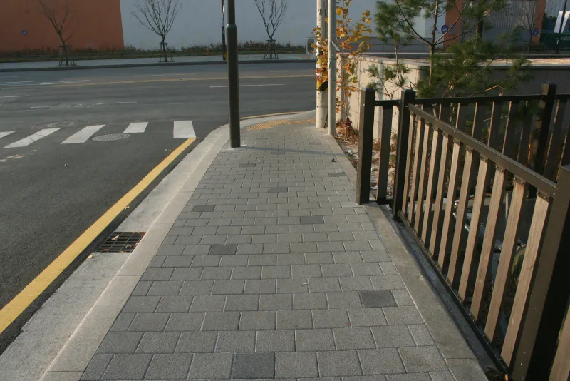 성수문화복지회관 인근 보도 모퉁이. 회색 블록 보도가 노란 연석 선과 검은 철제 난간 사이로 휘어지며 횡단보도 쪽으로 이어진다.