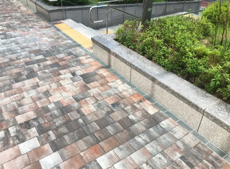 래미안 프리미어 팰리스 화단 옆 경사로. 여러 색이 섞인 블록 바닥 끝에 노란 점자블록과 화강석 계단이 보인다.