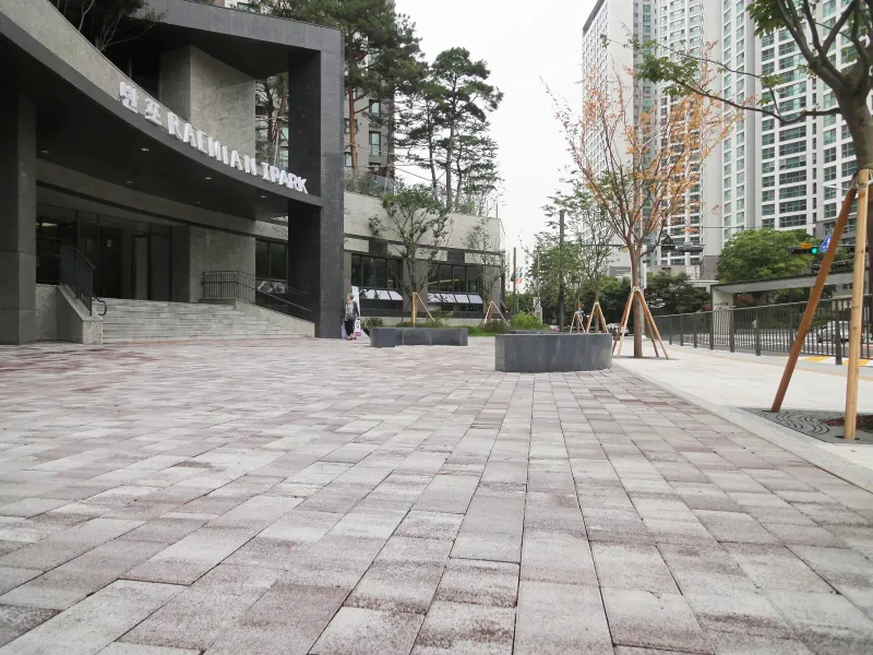 반포 래미안 아이파크 단지 정문 앞 광장. 연분홍·회색 톤 블록이 넓게 깔리고 뒤로 단지 이름이 걸린 문주와 고층 동이 서 있다.