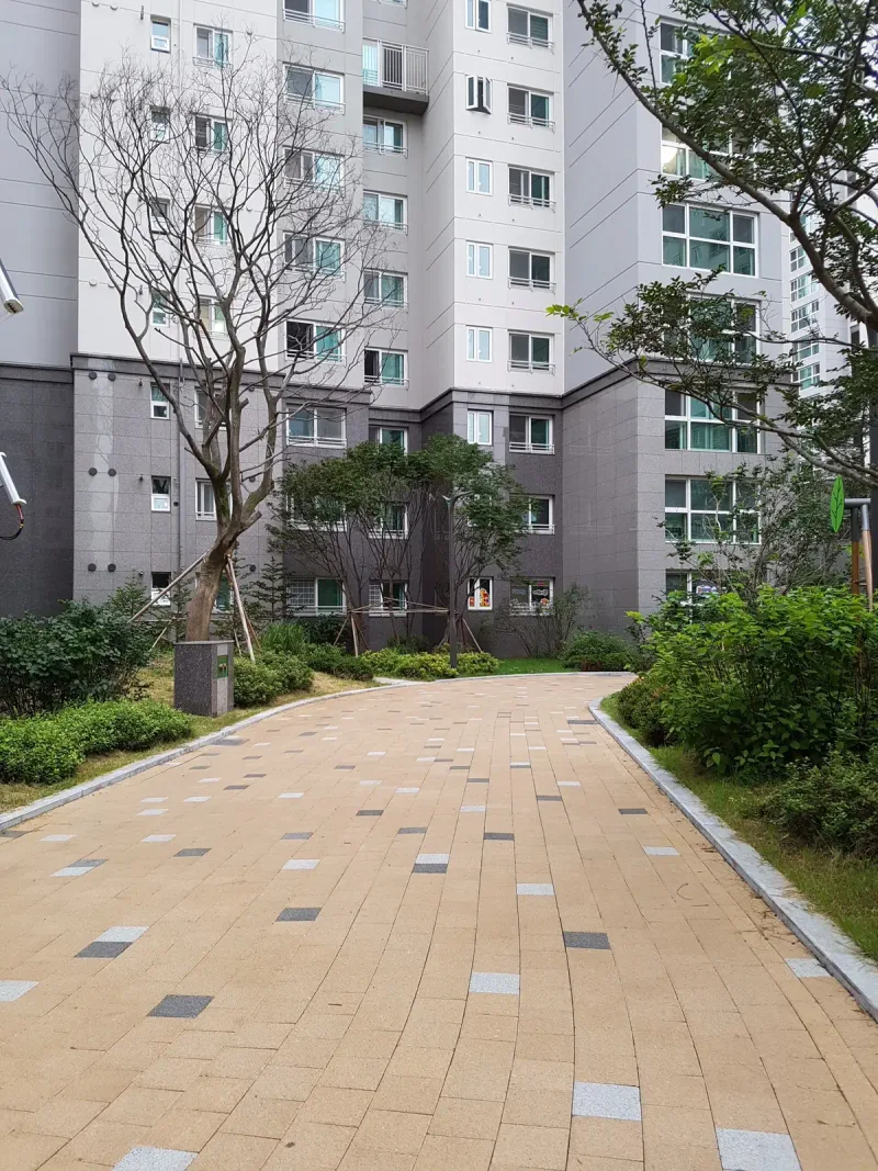 신길 래미안 단지 안 곡선 보행로 세로 사진. 베이지 블록에 짙은 블록이 드문드문 섞인 길이 화단 사이로 아파트 쪽으로 이어진다.