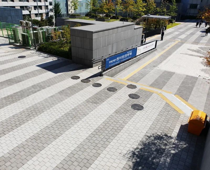중앙대학교 광장 내려다본 모습. 흰색·회색·짙은 회색 블록 줄무늬가 사선으로 이어지고 노란 선이 길을 안내한다.