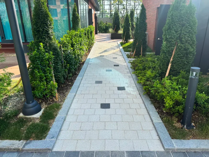 e편한세상 구성역 플랫폼시티 측백나무 화단 사이 좁은 보행로. 밝은 회색 블록 길 양옆에 경계석과 볼라드 조명이 있다.