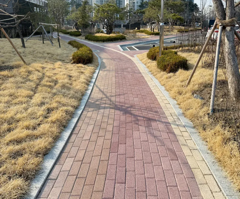 올림픽회관 마른 잔디밭 사이 보행로. 적갈색 블록 길 양쪽 가장자리에 베이지 블록 띠가 둘러져 있다.