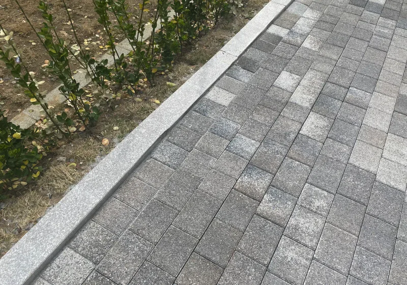 위례 자이 더 시티 보도 가장자리 근접. 회색·흰색·짙은 회색 직사각형 블록이 섞여 깔린 바닥 옆으로 화강석 경계석과 어린 관목이 줄지어 있다.