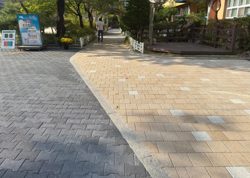 마포 염리초등학교 교문 안쪽. 짙은 회색 차도용 블록 통로 옆으로 베이지 블록 보행 구간이 넓게 깔리고 뒤로 교사와 나무 데크가 보인다.