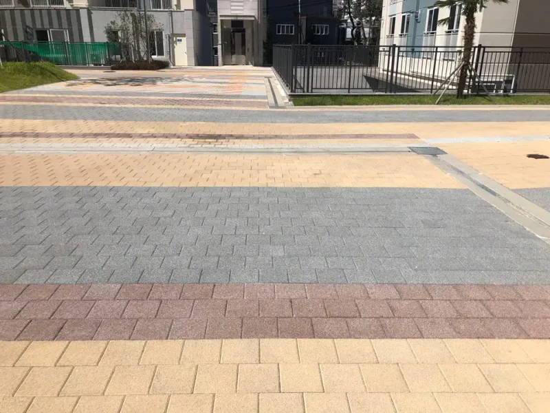 동래역 행복주택 단지 안 넓은 포장면. 베이지와 회색, 적갈색 블록이 가로 띠를 이루며 깔려 있고 뒤로 울타리와 주거동이 보인다.
