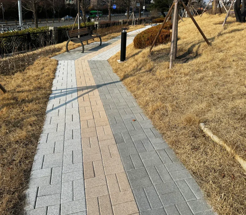 올림픽회관 벤치로 이어지는 좁은 산책로. 회색 블록 길 가운데로 베이지 블록 띠가 곧게 들어가 있다.