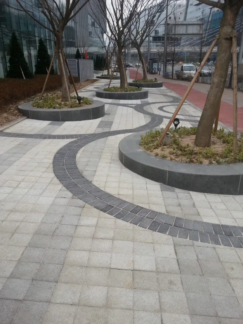 판교 SK 사옥 앞 광장을 세로로 담은 모습. 짙은 회색 블록 곡선 띠가 원형 화단 사이를 부드럽게 휘어 지나간다.