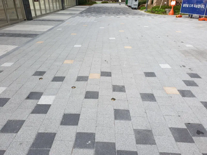 e편한세상 부산항 상가 앞 보행로. 연회색 블록 바탕에 짙은 회색·베이지 블록이 흩어진 무늬를 가까이 담았다.