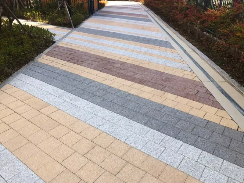 동래역 행복주택 단지 경사 보행로. 베이지·회색·적갈색·밝은 회색 블록이 넓은 사선 줄무늬로 번갈아 깔려 있고 양옆에 화단이 있다.