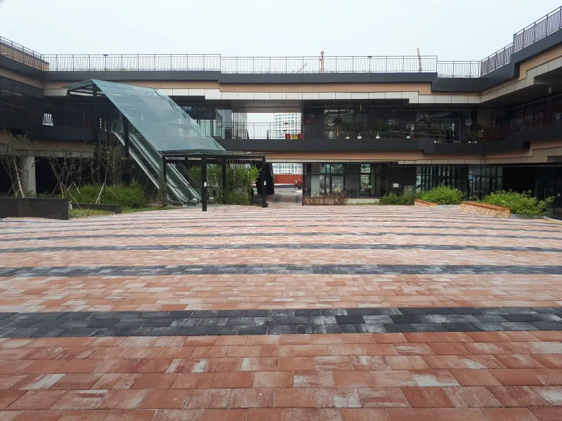 마치에비뉴 2차 상가 건물로 둘러싸인 광장을 지면에서 본 모습. 적갈색·분홍빛 블록 사이에 짙은 회색 띠가 가로로 반복된다.