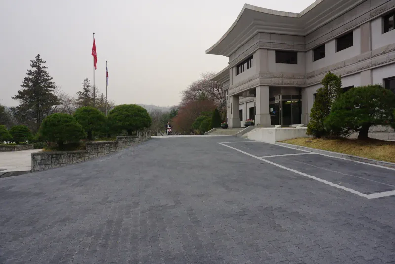 국립서울현충원 청사 옆 주차 공간. 짙은 회색 맞물림 차도블록이 넓게 깔린 바닥에 흰 주차선이 그어져 있고 오른쪽에 기와지붕 형태의 청사가 서 있다.