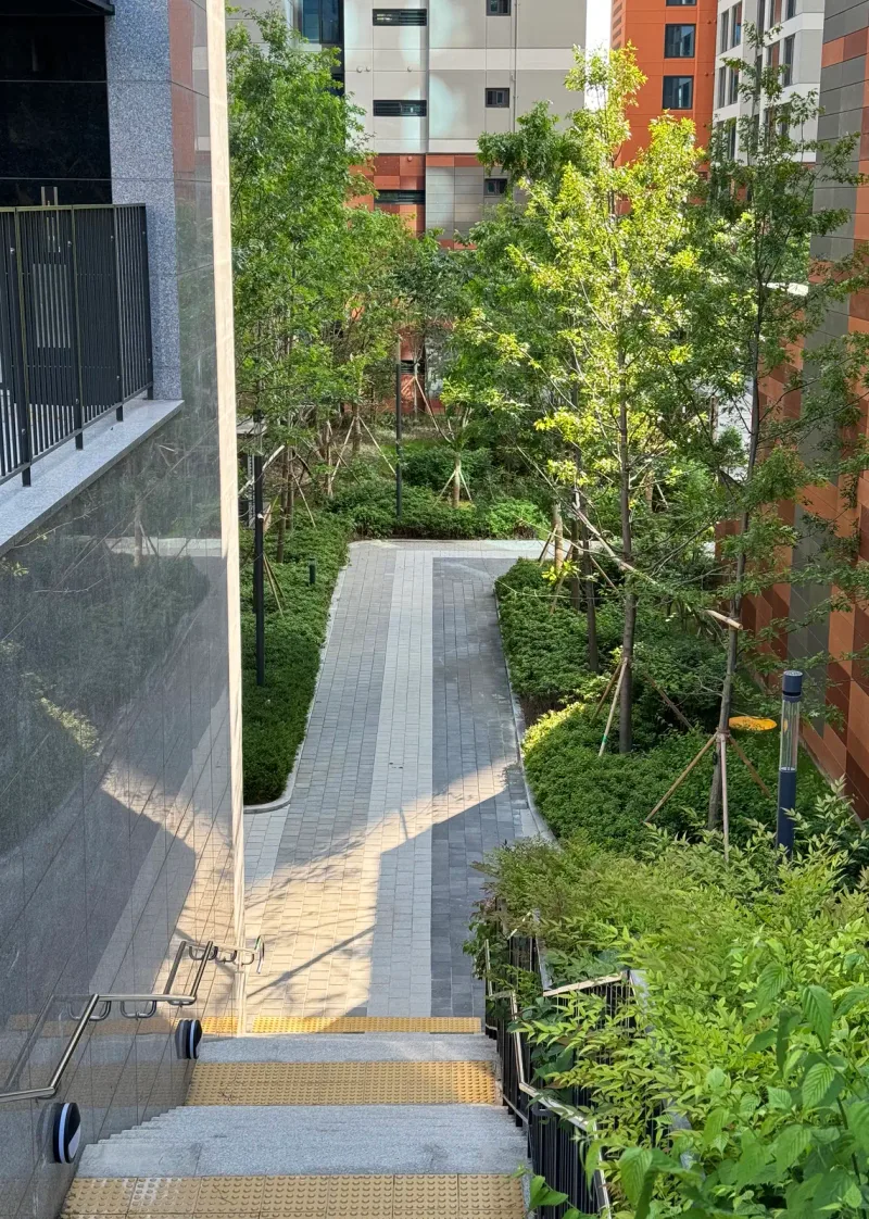 e편한세상 구성역 플랫폼시티 동 사이 산책로(세로 사진). 계단 위에서 내려다본 회색 블록 길이 나무와 관목 사이로 완만하게 휘어진다.