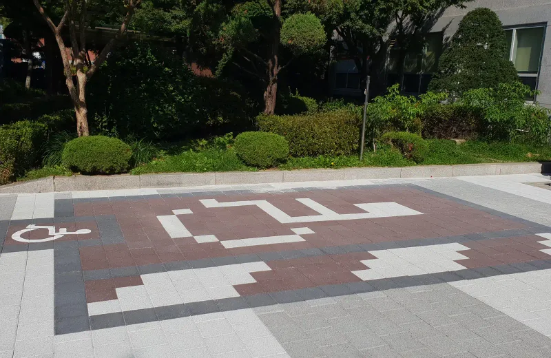 중앙대학교 주차 구역 바닥 근접. 적갈색 블록 사이에 흰 블록을 계단 모양으로 배열해 글자와 기호를 표현했다.