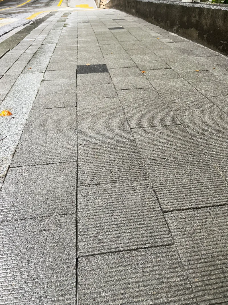 중구 보도유지공사 구간 보도 표면 근접. 가는 가로 줄무늬가 새겨진 회색 블록이 줄눈을 엇갈려 깔리고 가운데 검은 블록이 하나 박혀 있다.