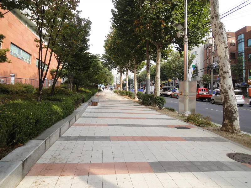숭실대학교 중문 앞 보도. 연회색 정사각 블록 바닥에 적갈색·짙은 회색 블록 줄이 가로로 반복되고 붉은 벽돌 건물과 플라타너스 가로수를 따라 길게 이어진다.