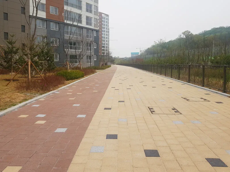 동탄2 아이파크 외곽 산책로. 적갈색과 베이지 두 가지 색 블록 길이 철제 울타리와 야산을 따라 길게 이어진다.