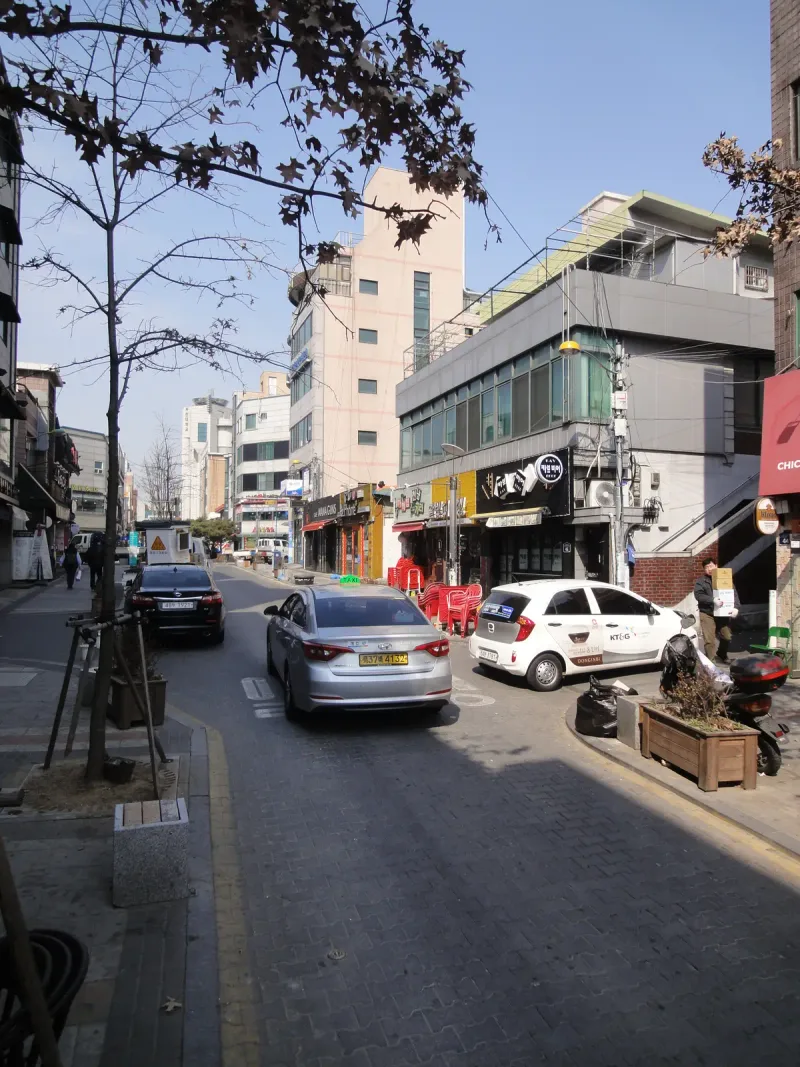 부천 차도블록 구간 상점가 차도. 승용차가 지나가는 블록 포장 도로 옆 보도에 화단과 가로수가 놓여 있다.