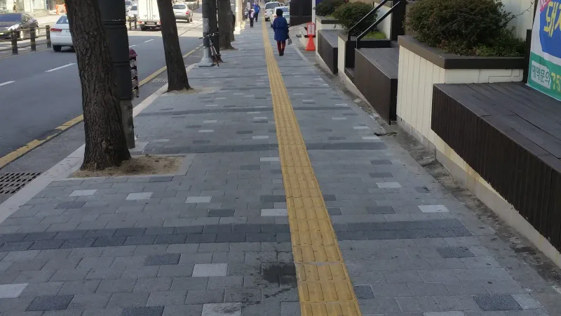 소방안전본부 일대 보도. 가로수 줄과 건물 앞 계단 사이로 회색 블록 보도가 뻗고 가운데 노란 점자블록이 길게 이어진다.